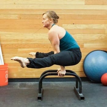 Sidney doing a straddle sit exercise on parallettes